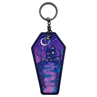 Coffin shaped keychain. Haunted house on front, coffin top on back. Haunted house is bordered up, spirits, and dead trees. Fence with a cat guards