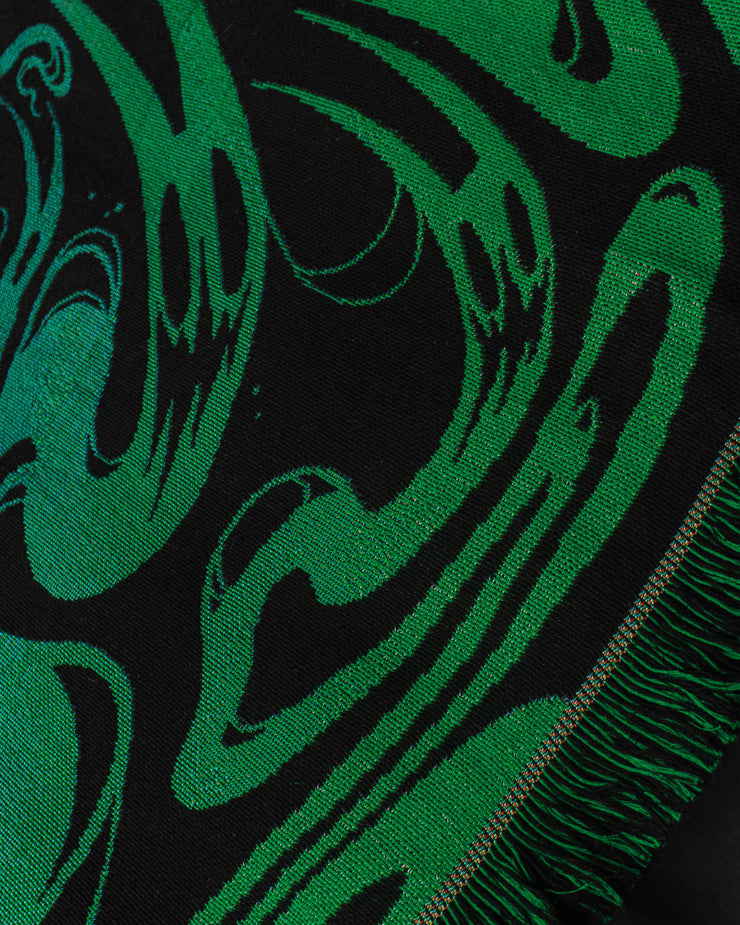 Underworld woven detail close up. featuring a deep green ghost face with a sharp mouth at the edge nearby tassels. 