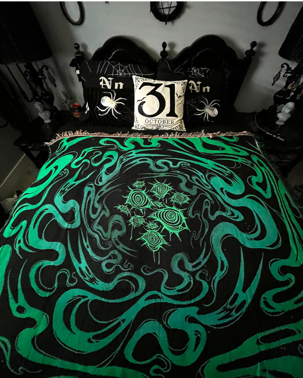 Underworld resting on a black bed with spider pillows against a white wall, surrounded by gothic room decor. Commission by LadyVampManor